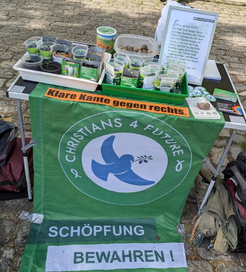 Ein Tisch mit Seedbombs und Infomaterial zum Mitnehmen. Als Tischdecke wurde eine Fahne von Chrstians4Future (\mit dem Aufdruck “Schöpfung bewahren") verwendet.