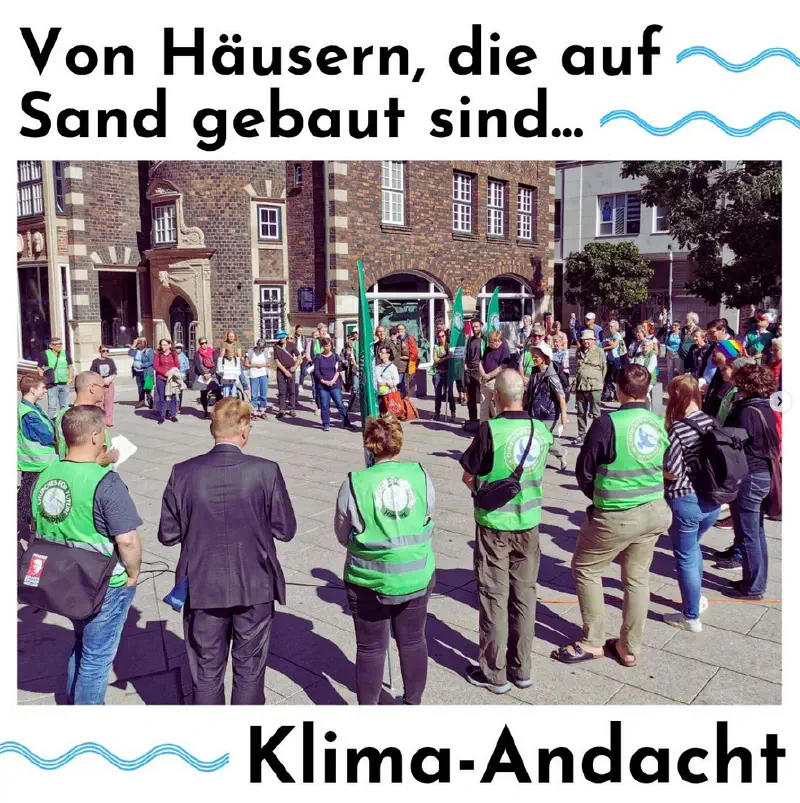 Teilnehmer:innen der Klimaandacht stehen in einem großen Kreis. Einige Personen tragen grüne Motto-Warnwesten und -Fahnen.