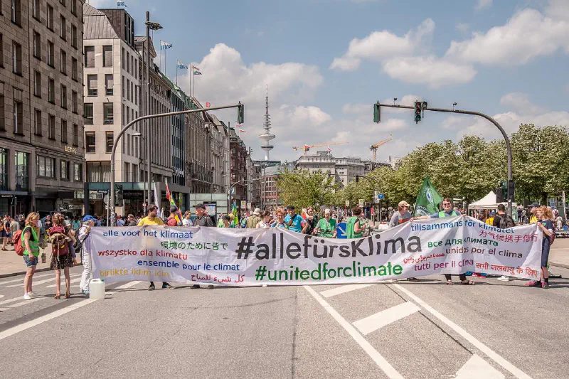 Demonstrationszug auf dem Jungfernstieg. Vorne wird ein großes Banner getragen, auf dem in vielen Sprachen steht: »alle fürs Klima«